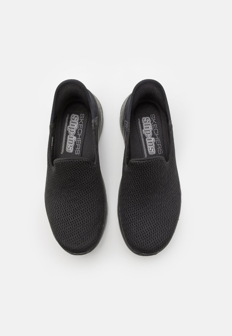 Scarpe slip-on nere in rete con suola in gomma liscia, dotate di pannelli elastici sui lati e marchio "SKECHERS slip-ins" sulla soletta.