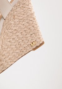 Sandalo con zeppa beige, sopra in juta intrecciata, dettagli in pelle e logo dorato. Superficie testurizzata e suola in gomma resistente.