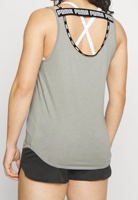 Grå sporttopp med rundad baksida, med ett svart och vitt logoband och korsade vita band under. Kombineras med svarta shorts.