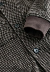 Dark brown and gray houndstooth coat with black buttons and a dark brown ribbed knit cuff on the sleeve.