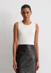 Weißes ärmelloses Oberteil mit rundem Halsausschnitt, kombiniert mit einem figurbetonten schwarzen Lederrock, glatte Textur und elegantes Design.