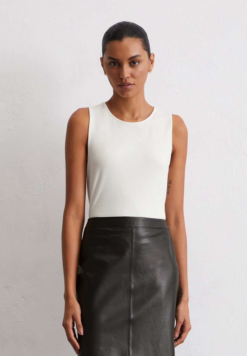 Weißes ärmelloses Oberteil mit rundem Halsausschnitt, kombiniert mit einem figurbetonten schwarzen Lederrock, glatte Textur und elegantes Design.