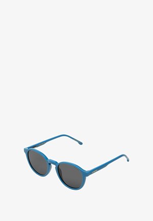 Lunettes de soleil rondes bleues avec des verres noirs et des branches fines, légèrement inclinées vers la droite sur un fond blanc.