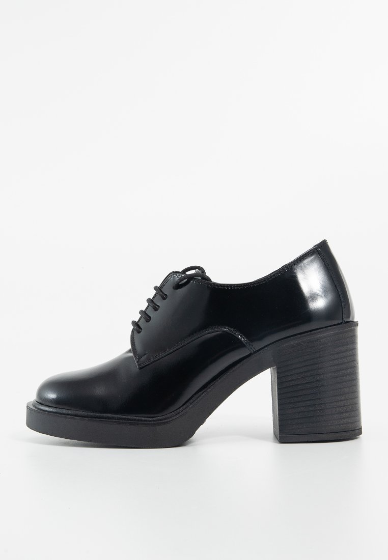 Chaussure en cuir verni noir avec un bout rond, un laçage, et un talon haut épais avec une semelle noire texturée.