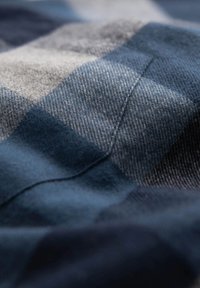 Tela a cuadros en azul y gris con una textura suave, que muestra una mezcla de áreas lisas y texturizadas, con detalles de costura visibles.
