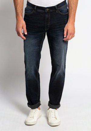 Jeans de mezclilla azul oscuro con corte ajustado, con decoloración ligera, diseño de cinco bolsillos y puños enrollados, combinados con zapatillas blancas.