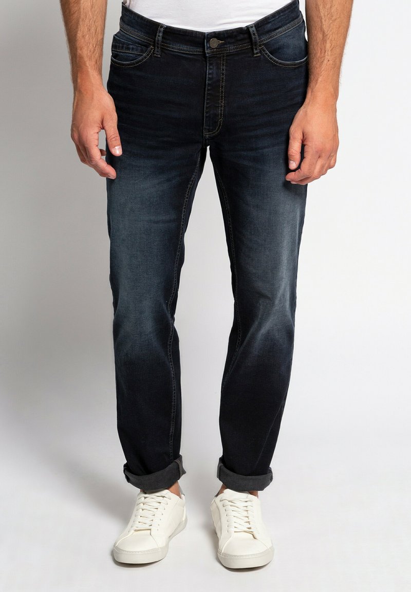 Jeans in denim blu scuro con vestibilità slim, caratterizzati da un leggero sbiadimento, design a cinque tasche e orli arrotolati, abbinati a sneakers bianche.