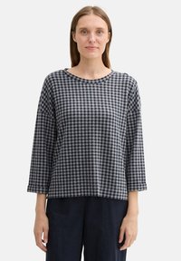 Top a scacchi bianchi e neri con scollatura rotonda, maniche lunghe e vestibilità rilassata. Tessuto morbido con una sottile texture.