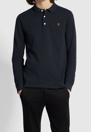 Polo bleu marine à manches longues en tissu texturé avec un col classique, trois boutons blancs et un petit logo jaune sur la poitrine.