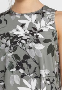 Sukienka bez rękawów z szarego materiału z botanicznym wzorem liści w czerni, bieli i odcieniach zieleni; gładka faktura; okrągły dekolt.