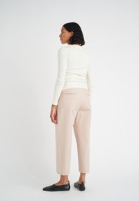 Långärmad ribbad krämfärgad topp, ljusrosa cropped-byxor och svarta platta skor. Enkelt design med subtila sömdetaljer bak på byxorna.