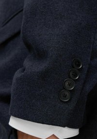 Navy-Wollblazerärmel mit vier schwarzen Knöpfen, strukturiertem Stoff und kontrastierendem weißen Hemdmanschette darunter.