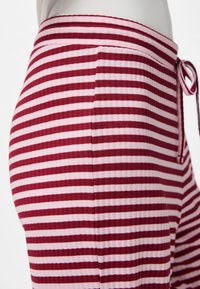 Gestreifte Hose mit horizontalen roten und pinken Streifen, weicher Textur, elastischem Bund und einer Schleifendetail an der Vorderseite.