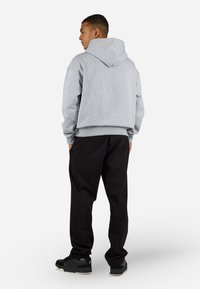 Grå hettegenser med kengurulomme og ribbestrikket kant, sammen med svarte joggebukser. Brukt med svarte sneakers.