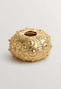 Objeto decorativo de oro, forma redonda con textura en relieve, patrones circulares y pequeños acentos elevados. Apertura central para exhibición.