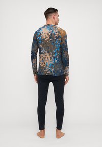 Bluza cu mânecă lungă în nuanțe de albastru, maro și bej, cu un model tie-dye, realizată dintr-un material moale. Asortată cu pantaloni negri mulati.