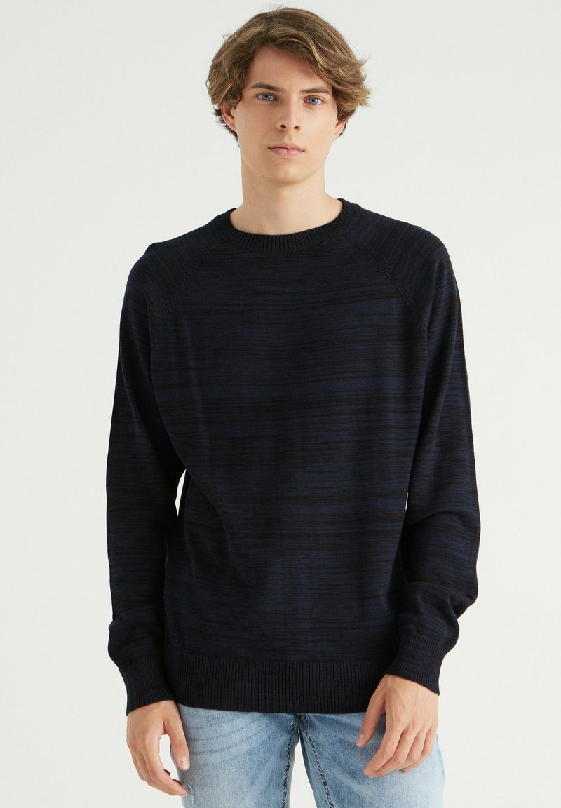 Suéter de punto azul marino con un patrón de rayas texturizado, cuello redondo acanalado y puños; corte relajado con mangas largas y detalles sutiles.