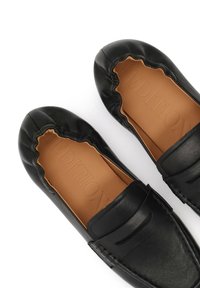 Mocassins noirs en cuir sans lacets avec bords élastiques froncés et semelles intérieures coussinées de couleur beige, vus en plongée sur un fond blanc.