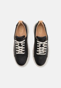 Sneakers neri in pelle con lacci bianchi, un accento in pelle beige sul tallone e una suola in gomma bianca, caratterizzati da una superficie liscia.