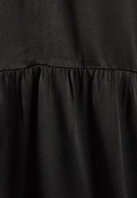 Tela negra con una textura suave, que presenta un volado fruncido en el dobladillo inferior. El material parece ligero y fluido.