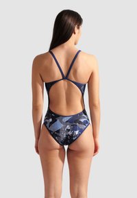 Maillot de bain une pièce en bleu foncé avec des motifs abstraits bleu clair et blancs. Présente un design à dos croisé et un découpe dans le dos.