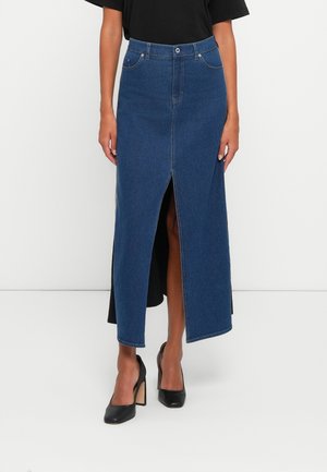 Mujer con falda midi vaquera azul con una abertura frontal, combinada con zapatos negros de tacón alto y una camiseta negra.