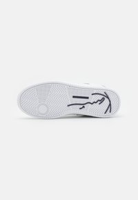 White sneaker sole with textured grip pattern, featuring a black outline of a logo and a circular reinforcement spot.