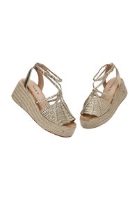 Sandalias de plataforma de oro trenzadas con un diseño de trenza, punta abierta y correas en el tobillo. La suela presenta un aspecto texturizado de yute natural.