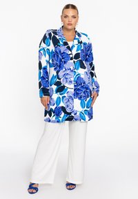 Langer floralem Mantel mit blau-weißem Design, das große blaue Blumen und grüne Blätter zeigt. Enthält Knöpfe und einen spitzen Kragen. Wird über weißen Hosen getragen.