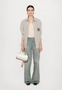 Striped button-up shirt with brown embroidery, beige tank top, light blue wide-leg jeans, and a white handbag with a silver strap.