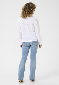 Camicia bianca a maniche lunghe con spalle a sbuffo, abbinata a jeans svasati blu chiaro con dettagli di cucitura sulle tasche posteriori.