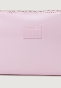 Różowa kosmetyczka o miękkiej teksturze z zamkiem błyskawicznym, z wytłoczonym logiem "TOMMY JEANS" na przodzie. Kompaktowy design.