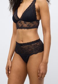 Černá krajková podprsenka s květinovým vzorem a vroubkovanými okraji, doplněná o sladěné krajkové a saténové kalhotky s jemnou mašličkou.