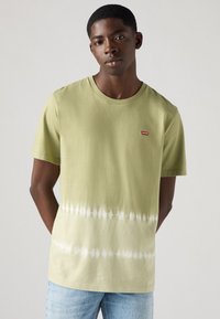Alyvuogių žalumo spalvos dažyta T-shirt su apvaliu kaklu ir trumpomis rankovėmis. Viršutiniame kairiajame kampe yra mažas raudonas Levi's logotipas.