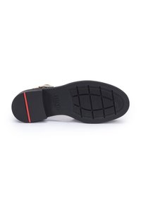 Suela de zapato negra con un patrón texturizado, con una franja de acento roja cerca del talón y una impresión de logo de la marca.
