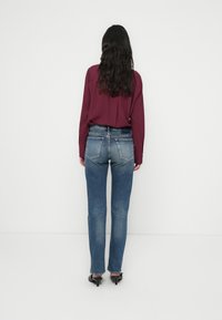 Blugi din denim albastru cu croială slim, având o spălare estompată, cinci buzunare și închidere cu nasture, asortați unei bluze burgundy cu mâneci lungi.