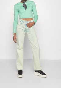 Mint green cropped long-sleeve top with logo, paired with light wash, relaxed-fit jeans. Black sneakers feature white soles and laces.