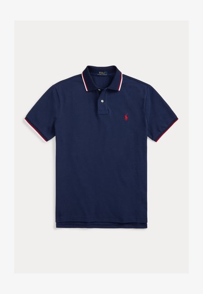 Camisa polo azul marinho em algodão, com um colarinho listrado em vermelho e branco, com três botões e um pequeno logotipo bordado no peito.