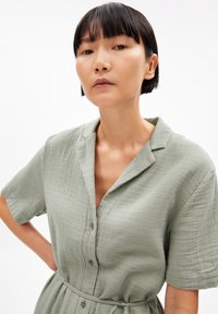 Abito camicia verde chiaro a maniche corte in tessuto testurizzato con parte anteriore a bottoni, colletto e vita legata.