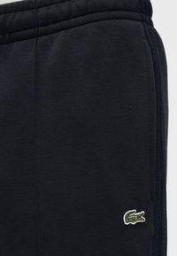 Σκούρο μπλε φόρμα παντελόνι από απαλό ύφασμα, με φερμουάρ στο πλάι και μικρό πράσινο κεντητό λογότυπο κροκοδείλου στο πόδι.