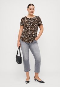 Majica kratkih rukava s uzorkom leoparda u smešanoj i crnoj boji, u kombinaciji s kratkim sivim trapericama i crnim ravnim cipelama, uz elegantnu torbicu.