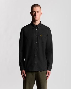 Chemise noire avec col boutonné, manches longues et une poche ornée d'un petit logo jaune. Fabriquée en tissu lisse, avec des boutons blancs.