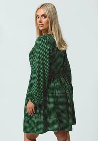 Vihreä ruudullinen mekko, jossa on pitkät puffihihat, rento malli ja rypytetty vyötärö, valmistettu kevyestä kankaasta.