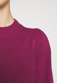 Pull tricoté fuchsia avec une finition côtelée, doté d'un col rond et de détails à épaules bouffantes. Texture douce et épaisseur moyenne.
