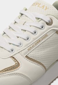 Baskets blanches perforées avec lacets blancs, coutures dorées et texte "REPLAY DENIM LOVERS" sur le panneau latéral.