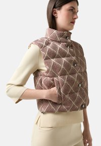 Czerwona i kremowa kamizelka puchowa w wzory, z wysokim kołnierzem, pięcioma zatrzaskami i bocznymi kieszeniami. Żebrowany wykończenie na dole i w otworach na ramiona.