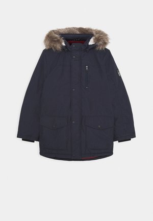 Parka marine avec une garniture en fausse fourrure sur la capuche, poche poitrine zippée et deux grandes poches avant. Comprend une doublure intérieure rouge.