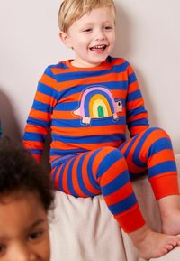 Stribede pyjamas i blå og orange med en skildpadde med et regnbuens skalsdesign. Fremstillet af blødt stof med kontrastfarvede manchetter og taljebånd.