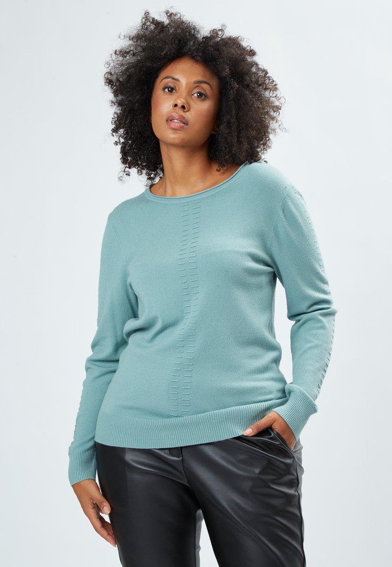 Maglione verde acqua realizzato in materiale morbido, con un colletto a coste e una texture dettagliata lungo il centro; abbinato a pantaloni in pelle neri.