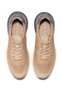 Béžové perforované tenisky s texturovaným povrchem, plochými tkaničkami a námořnickou akcentovanou patou. Vybavené krémovou podrážkou a brandingem na jazyku.